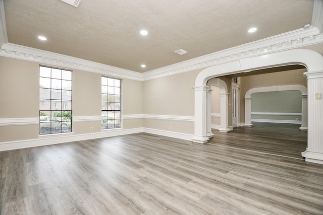 empty room with a textured ceiling, crown molding, hardwood / wood-style flooring, and decorative columns