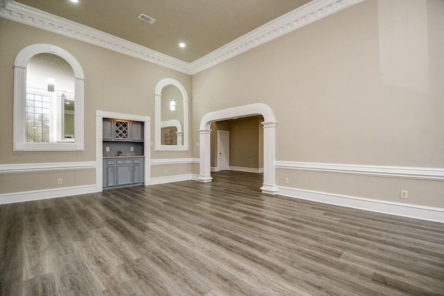 unfurnished living room featuring dark wood-type flooring, ornamental molding, and indoor bar