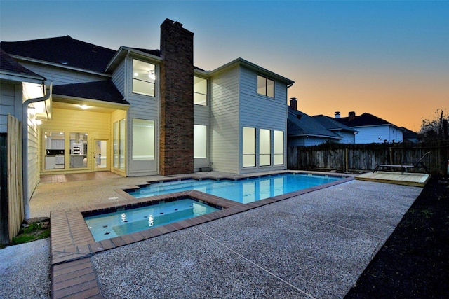 back house at dusk featuring a pool with hot tub and a patio