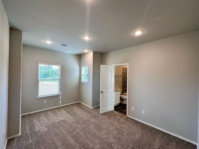 unfurnished bedroom featuring ensuite bath and dark carpet