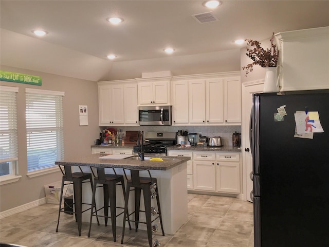 kitchen featuring a kitchen bar, white cabinetry, vaulted ceiling, appliances with stainless steel finishes, and an island with sink