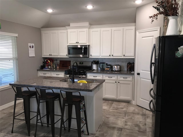 kitchen featuring lofted ceiling, appliances with stainless steel finishes, white cabinetry, a kitchen island with sink, and a kitchen breakfast bar