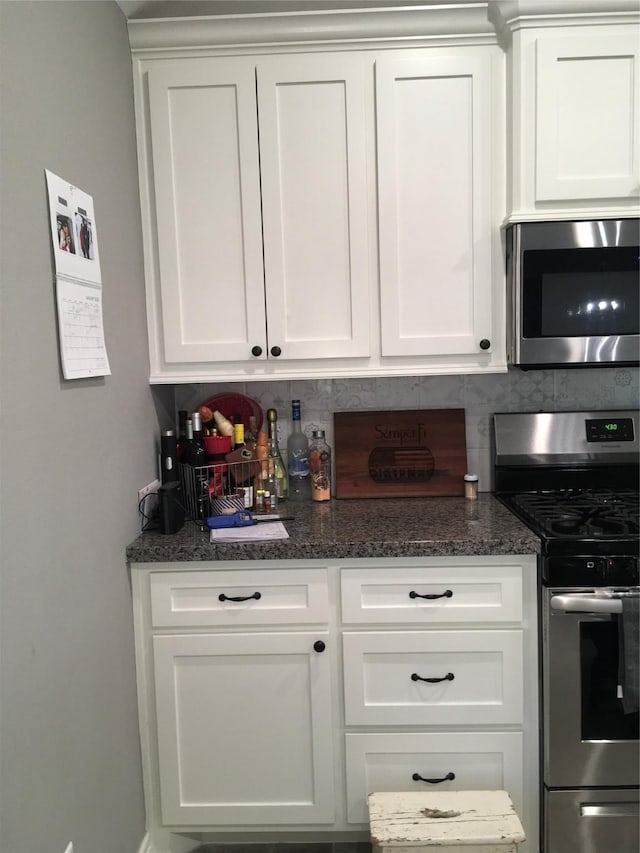 bar with white cabinetry, appliances with stainless steel finishes, dark stone countertops, and backsplash