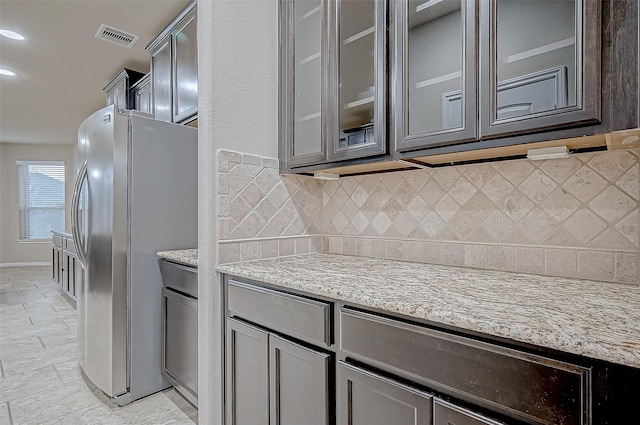 kitchen with stainless steel refrigerator, tasteful backsplash, and light stone countertops