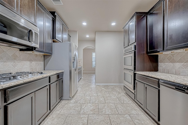 kitchen with tasteful backsplash, stainless steel appliances, light stone countertops, and dark brown cabinetry