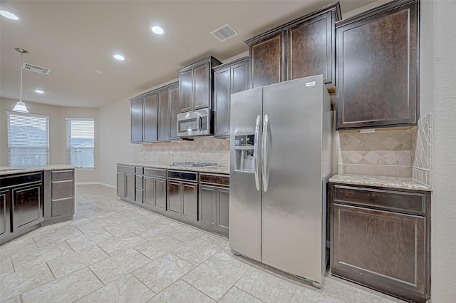 kitchen featuring stainless steel appliances, hanging light fixtures, light stone countertops, decorative backsplash, and dark brown cabinets