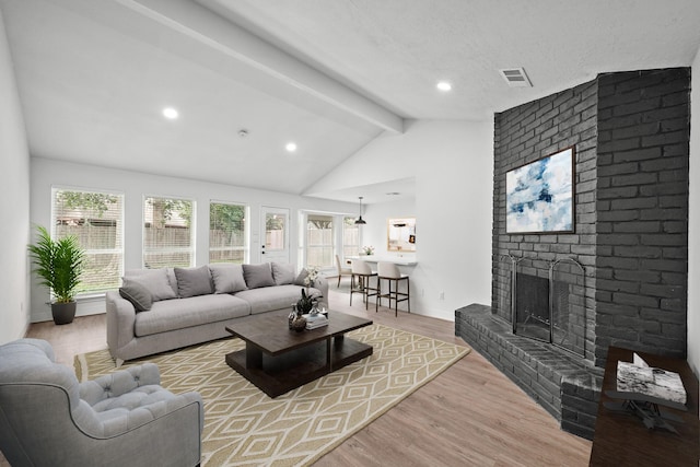 living room featuring a brick fireplace, vaulted ceiling with beams, light hardwood / wood-style flooring, and plenty of natural light