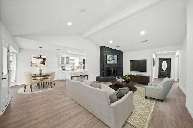 living room with a brick fireplace, light wood-type flooring, and lofted ceiling with beams