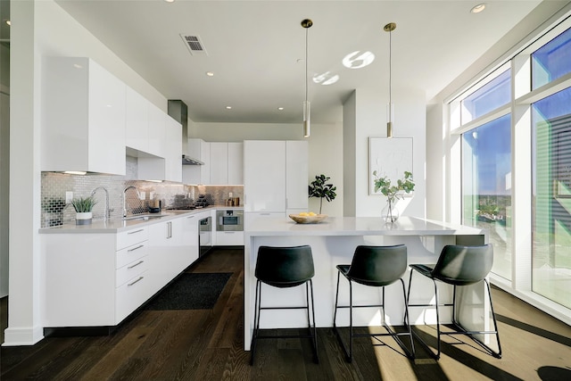 kitchen with sink, decorative light fixtures, white cabinetry, wall chimney range hood, and appliances with stainless steel finishes