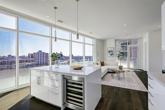 kitchen featuring white cabinetry, an island with sink, beverage cooler, hanging light fixtures, and floor to ceiling windows