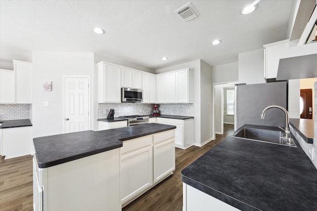 kitchen featuring dark wood-type flooring, stainless steel appliances, a kitchen island with sink, white cabinetry, and sink