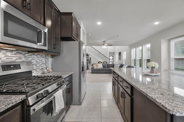 kitchen featuring light stone countertops, dark brown cabinetry, appliances with stainless steel finishes, decorative backsplash, and light tile patterned floors