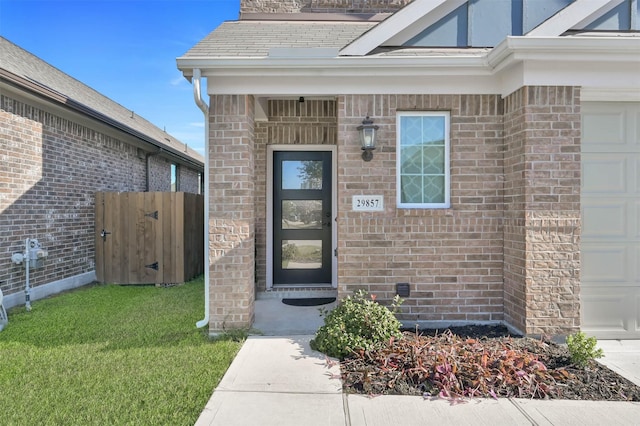 view of exterior entry with a garage and a lawn