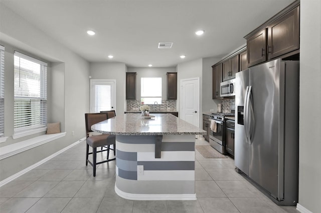 kitchen featuring a kitchen island, stainless steel appliances, a healthy amount of sunlight, tasteful backsplash, and light stone counters