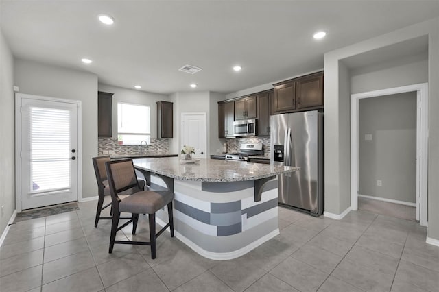 kitchen featuring a kitchen island, light stone countertops, a kitchen breakfast bar, stainless steel appliances, and dark brown cabinets