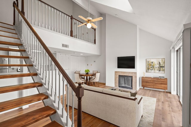 living room with ceiling fan, light wood-type flooring, high vaulted ceiling, and a fireplace