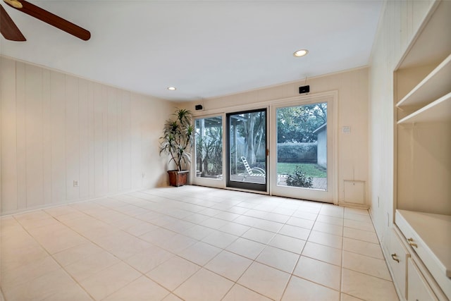 unfurnished room with light tile patterned floors, wooden walls, and ceiling fan