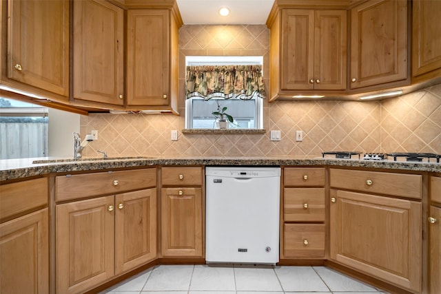 kitchen with sink, light tile patterned floors, white dishwasher, tasteful backsplash, and stone countertops