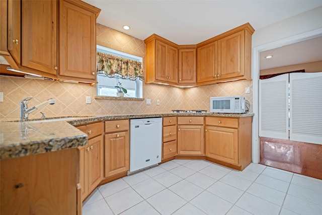 kitchen with sink, white appliances, light stone countertops, and backsplash