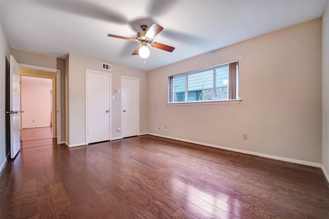 unfurnished bedroom featuring multiple closets, dark wood-type flooring, and ceiling fan