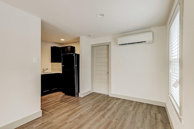 kitchen with sink, black fridge, light wood-type flooring, and a wall unit AC