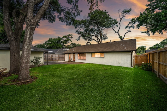 back house at dusk with a patio area and a lawn