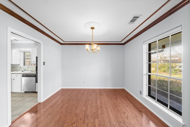 unfurnished dining area with an inviting chandelier, sink, ornamental molding, and light wood-type flooring