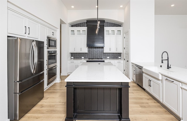 kitchen with appliances with stainless steel finishes, light stone countertops, white cabinets, decorative light fixtures, and sink