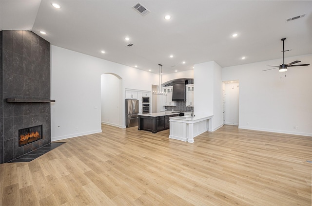 kitchen with decorative light fixtures, white cabinetry, a tiled fireplace, light hardwood / wood-style floors, and appliances with stainless steel finishes