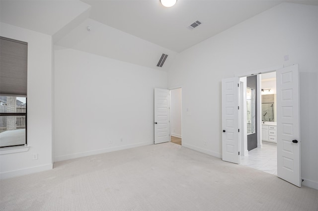 unfurnished bedroom with light colored carpet, high vaulted ceiling, and ensuite bath