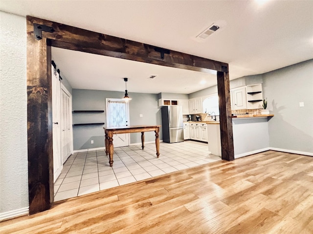 kitchen with light hardwood / wood-style floors, kitchen peninsula, stainless steel refrigerator, hanging light fixtures, and white cabinets