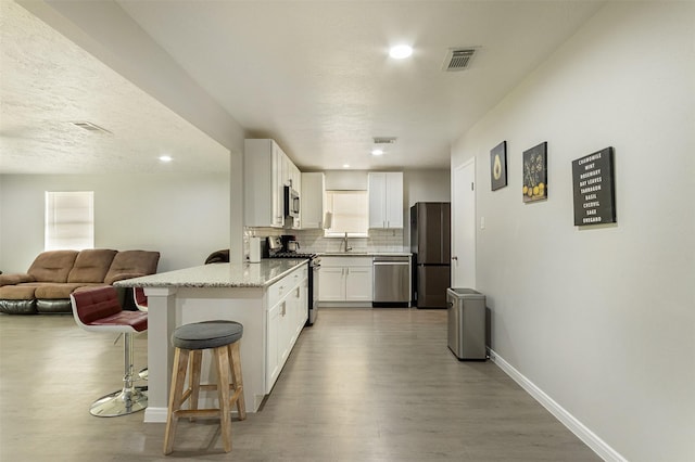 kitchen with light stone countertops, stainless steel appliances, backsplash, white cabinets, and a kitchen breakfast bar