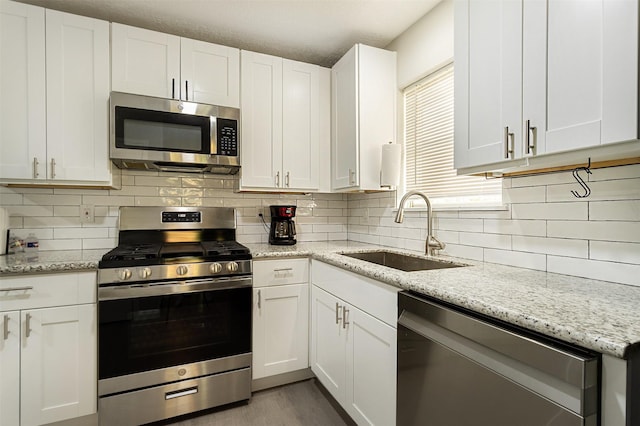 kitchen featuring appliances with stainless steel finishes, light stone countertops, white cabinets, backsplash, and sink