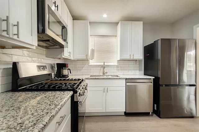 kitchen with stainless steel appliances, white cabinets, sink, and light stone counters