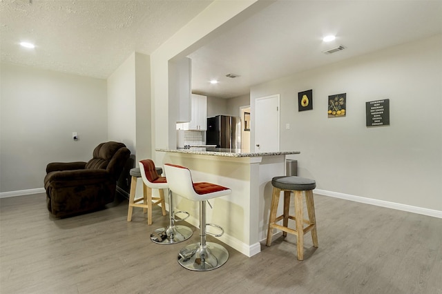 kitchen featuring kitchen peninsula, a breakfast bar, light wood-type flooring, white cabinetry, and stainless steel refrigerator