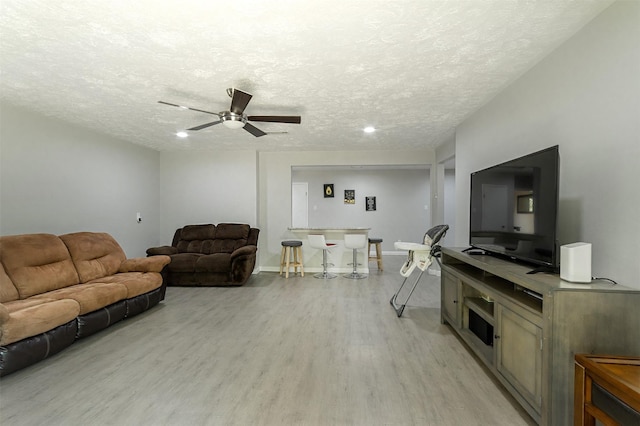 living room featuring a textured ceiling, light wood-type flooring, and ceiling fan