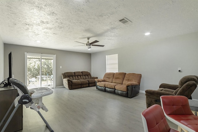 living room with ceiling fan, light wood-type flooring, and a textured ceiling