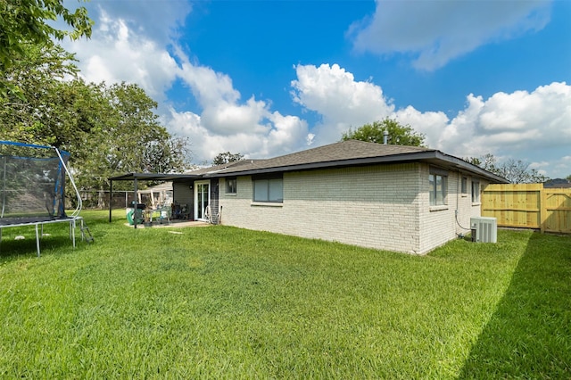 rear view of house featuring a yard, central AC unit, and a trampoline