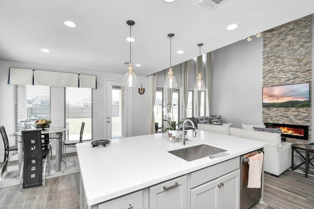 kitchen with an island with sink, a fireplace, sink, white cabinetry, and decorative light fixtures