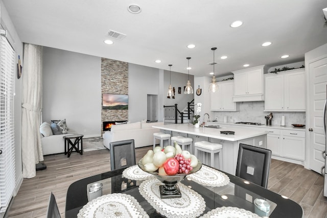 kitchen with white cabinets, pendant lighting, an island with sink, and a stone fireplace