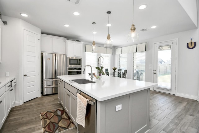 kitchen featuring stainless steel appliances, an island with sink, hanging light fixtures, sink, and white cabinetry