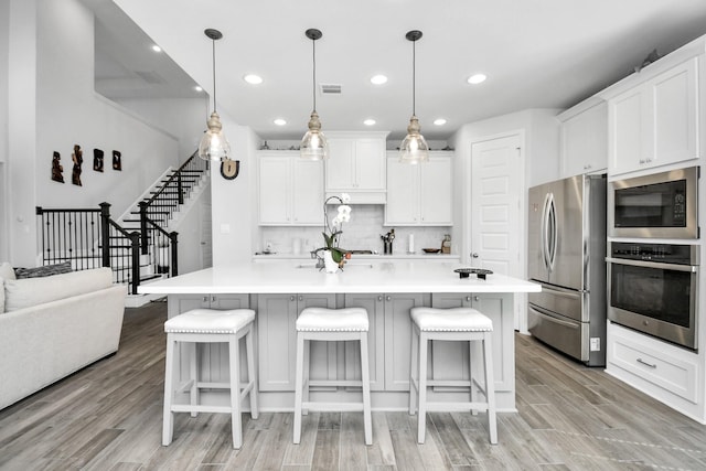 kitchen with light hardwood / wood-style flooring, decorative light fixtures, decorative backsplash, white cabinets, and appliances with stainless steel finishes