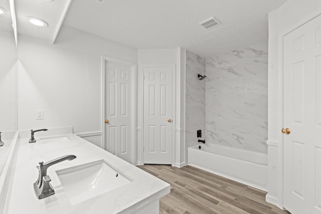 full bathroom with double vanity, visible vents, shower / tub combination, wood finished floors, and a sink