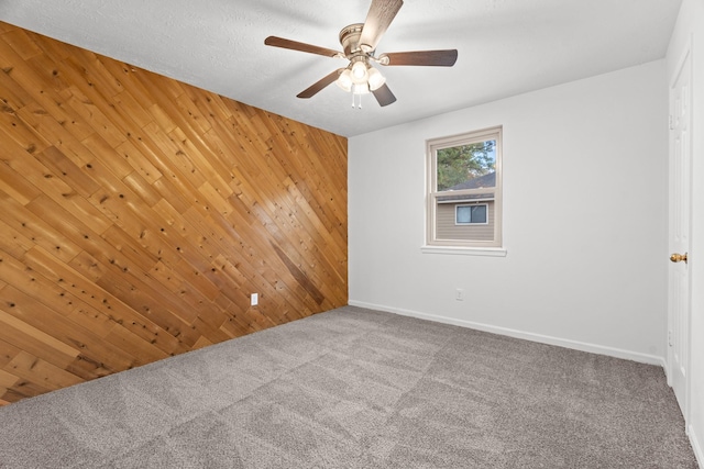 carpeted empty room with a ceiling fan, baseboards, wooden walls, and a textured ceiling