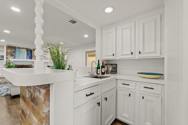 kitchen featuring visible vents, dark wood-style floors, a peninsula, white cabinetry, and a sink