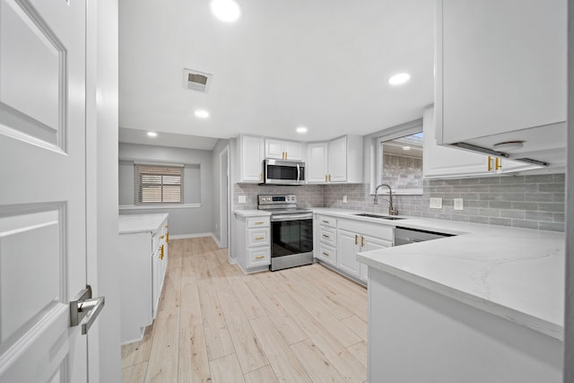 kitchen with light stone countertops, white cabinetry, appliances with stainless steel finishes, and sink