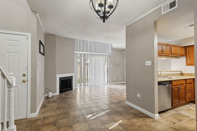 interior space with light tile patterned floors, a textured ceiling, sink, an inviting chandelier, and stainless steel dishwasher