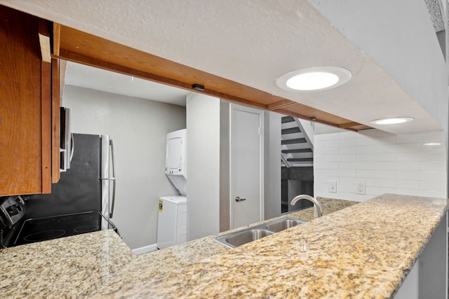 kitchen featuring light stone countertops, stainless steel range with electric cooktop, stacked washer / drying machine, backsplash, and sink