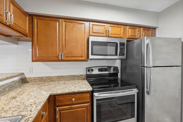 kitchen with backsplash, light stone counters, and appliances with stainless steel finishes