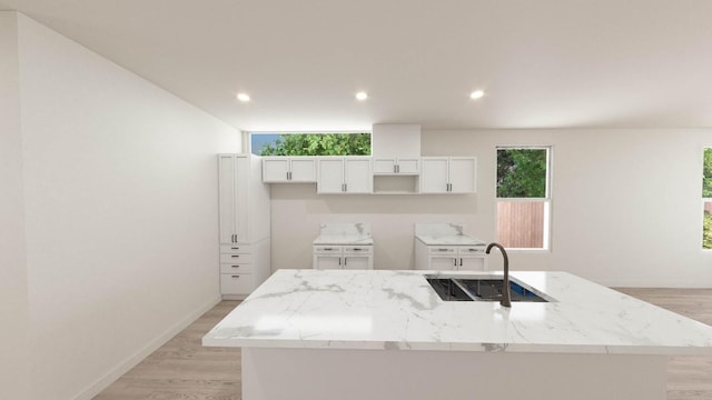 kitchen featuring sink, white cabinetry, light stone counters, and a center island with sink